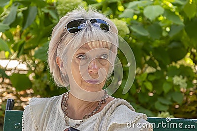 Portrait of an elderly thoughtful woman 60-65 years old on a blurred background of a green city park. Stock Photo