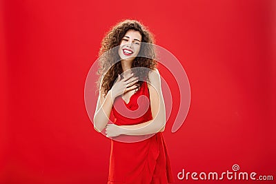 Portrait of elegant pleased and grateful charming caucasian woman with curly hairstyle holding palm on chest smiling and Stock Photo
