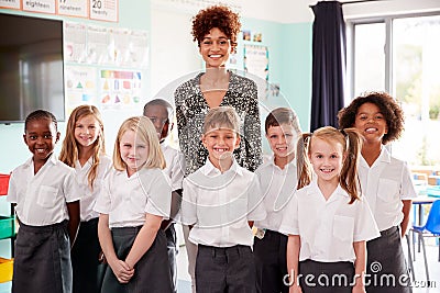 Portrait Of Elementary School Pupils Wearing Uniform Standing In Classroom With Female Teacher Stock Photo