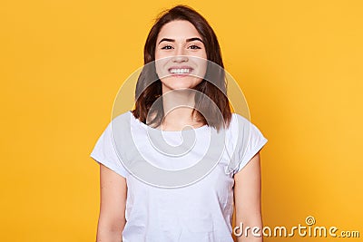 Portrait of emotive good looking caucasian woman laughs while looking directly at camera and standing against yellow background. Stock Photo