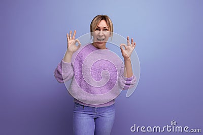 portrait of energetic yawning pleasant blond woman in lavender sweater on purple background with copy space Stock Photo