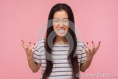 Portrait of enraged furious girl with long hair in striped t-shirt standing with clenched teeth and raised hands Stock Photo