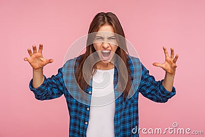 Portrait of enraged girl in checkered shirt with furious crazy grimace raising hands and shouting in hatred Stock Photo