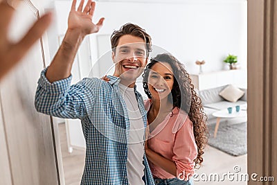 Happy couple inviting people to enter home, giving high five Stock Photo