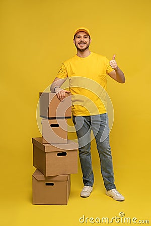 Portrait of excited delivery man in yellow uniform holding paper box isolated over yellow background. Stock Photo