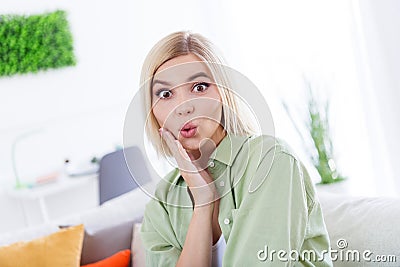 Portrait of excited funny lady wearing khaki shirt touching cheek pouted lips surprisingly reaction when sit indoors on Stock Photo