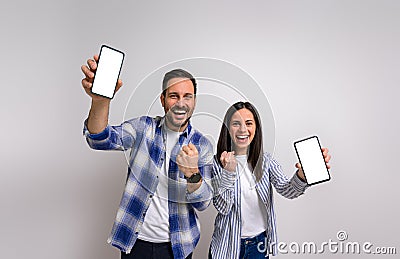 Portrait of excited girlfriend with boyfriend laughing and pumping fists while showing mobile phones. Ecstatic young couple Stock Photo