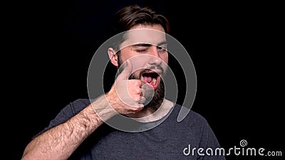 Portrait of excited man with opened mouth giving thumbs-up and winking against black background. Smiling bearded young Stock Photo