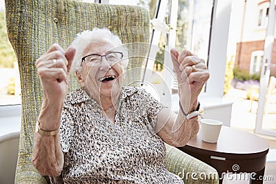 Portrait Of Excited Senior Woman Sitting In Chair In Lounge Of Retirement Home Stock Photo