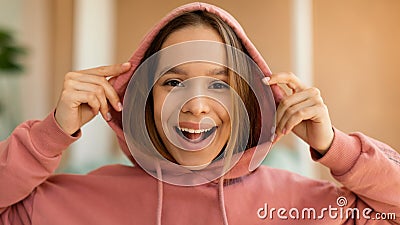 Portrait of excited tenage girl wearing hood and smiling at camera, posing indoors at home interior Stock Photo
