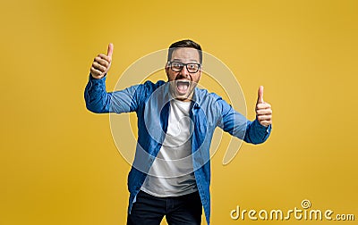 Portrait of exited businessman showing thumbs up and screaming in joy against yellow background Stock Photo