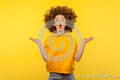 Portrait of extremely surprised girl in urban style hoodie jumping with her messy curly hair up, yellow background Stock Photo