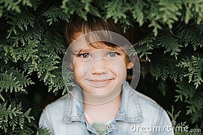 Portrait of the face of a cute little happy caucasian candid healthy five year old kid boy surrounded by branches and leaves of gr Stock Photo