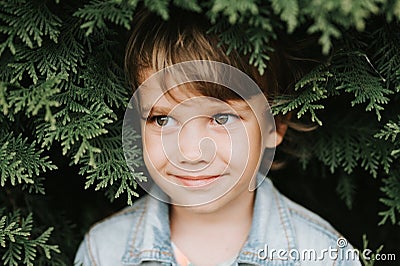 Portrait of the face of a cute little happy caucasian candid healthy five year old kid boy surrounded by branches and leaves of gr Stock Photo