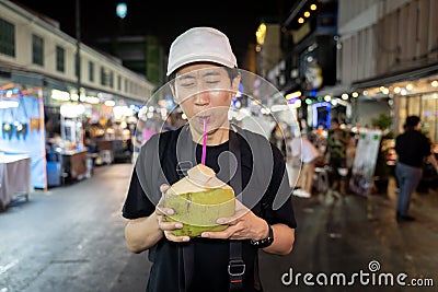 Portrait face of thirsty Asian solo hipster traveller holding a coconut drink on street in Bangkok, Thailand. Stock Photo