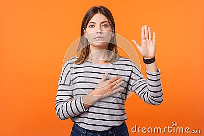 Portrait of faithful beautiful young woman with brown hair in long sleeve striped shirt. indoor studio shot isolated on orange Stock Photo