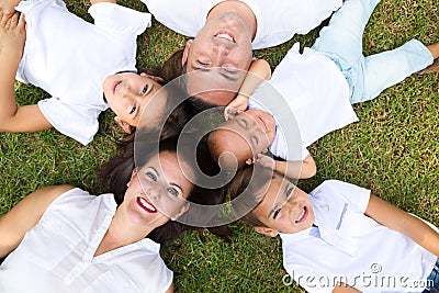 Portrait of a family of five, father, mother and children lying on the fresh grass looking at the camera. It is an example of a Stock Photo