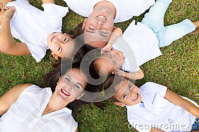 Portrait of a family of five, father, mother and children lying on the fresh grass looking at the camera. It is an example of a Stock Photo