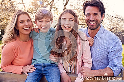 Portrait Of Family On Summer Walk Sitting On Wooden Fence In Countryside Stock Photo