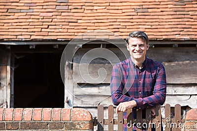 Portrait Of Farmer Looking Over Wall Of Farm Building Stock Photo