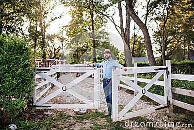 A portrait of farmer walking outdoors on family farm, opening gate. Stock Photo