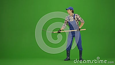 Portrait of farmer in working clothing on chroma key green screen. Gardener standing holding pitchfork for collecting Stock Photo