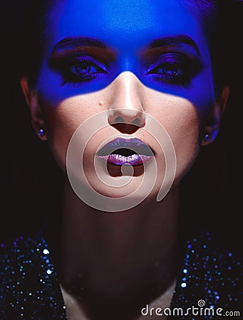 Portrait of fashion girl with stylish makeup and blue neon light on her face on the black background in the studio Stock Photo