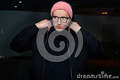 Portrait of fashionable casual young man standing on dark abstract background and holding his hood. Stock Photo