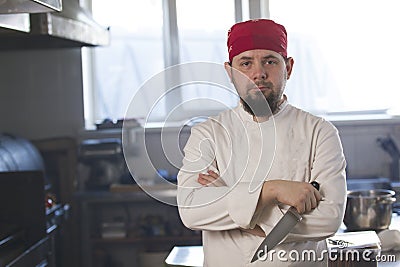 Portrait of a fashionable chef in bandana holding a knife in a kitchen Stock Photo