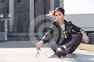 Portrait of fashionable impudent blonde girl with eye glasses wearing a rock black style outdoors in the city. Stock Photo