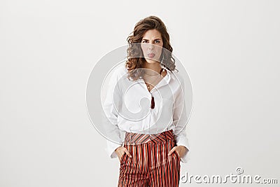 Portrait of fashionable slender european girl with curly hair, holding hands in pockets of striped pants, making faces Stock Photo