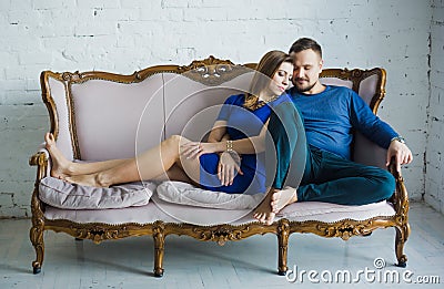 Portrait of a fashionable stylish couple sitting together with bare feet on the couch in the living room, embracing, smiling, Stock Photo