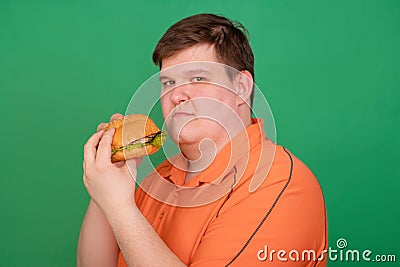 Portrait of a fat guy with a big hamburger in his hands, isolated on a green background. Chroma key, green screen Stock Photo
