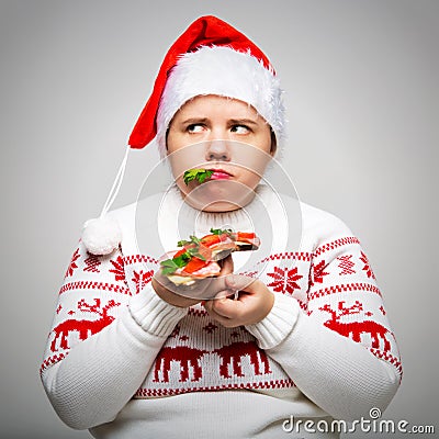 Portrait of a fat woman with a large sandwich in her hands. She is wearing a festive Christmas sweater and Santa hat Stock Photo