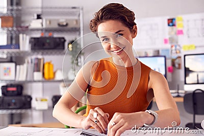 Portrait Of Female Architect At Desk In Office Measuring Plan Or Blueprint With Ruler Stock Photo