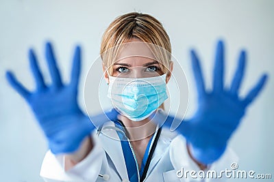 female doctor with a medical mask showing hands to camera while wearing a blue nitrile gloves over white background Stock Photo
