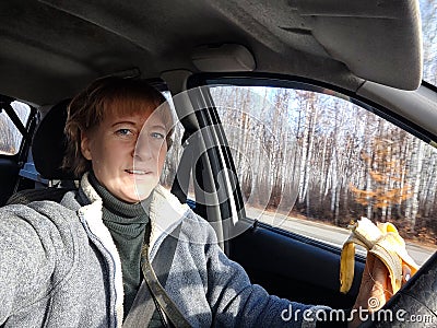 Portrait of female driver in solo journey. Adult mature middle aged woman holding steering wheel and banana. Eating Stock Photo