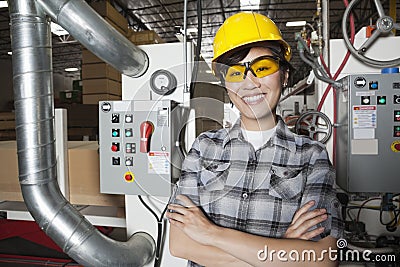 Portrait of female industrial worker smiling while standing in factory with machines in background Stock Photo