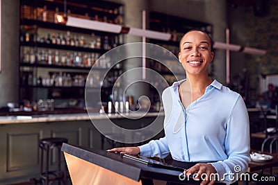 Portrait Of Female Owner Of Restaurant Bar Standing At Counter Using Digital Tablet Stock Photo