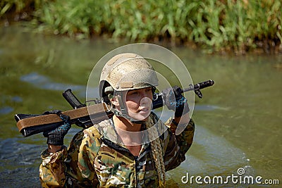 Portrait of fit military female holding weapon rifle in hands in river, posing alone. Confident strong athlete lady Stock Photo