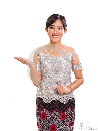 Portrait of friendly smiling Southeast Asian girl wearing kebaya and batik costume giving direction side way, isolated on white b Stock Photo