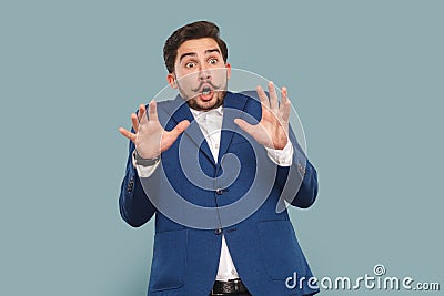 Frighten shocked man with mustache standing with raised arms, looking with big scared eyes. Stock Photo