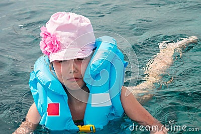 Portrait of a frightened child in the sea. A baby is saved after a disaster. A sad little girl in a life jacket tries to swim in Stock Photo