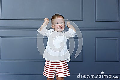 The portrait of a frustrated little girl holds her hands up, wearing a white blouse and red shorts Stock Photo
