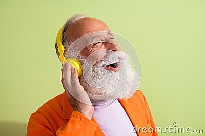 Portrait of funky eccentric grandfather closed eyes touch headphones wear orange suit isolated on green color background Stock Photo