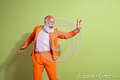 Portrait of funky eccentric grandfather dancing empty space wear orange suit isolated on green color background Stock Photo