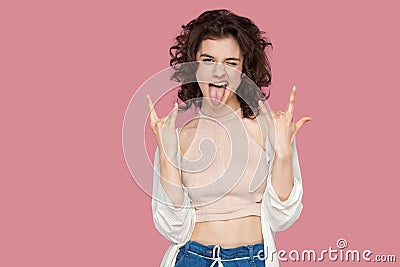 Portrait of funny beautiful brunette young woman with curly hairstyle in casual style standing with rock sign and looking at Stock Photo