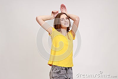 Portrait of funny carefree attractive teenager girl in yellow T-shirt showing bunny ears gesture and Stock Photo