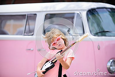 Portrait of a funny child with pink glasses practicing a song during a guitar lesson on street. Music concept, kids Stock Photo