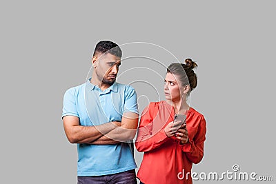 Portrait of funny resentful man in casual wear looking disapprovingly at woman using cellphone. isolated on gray background Stock Photo